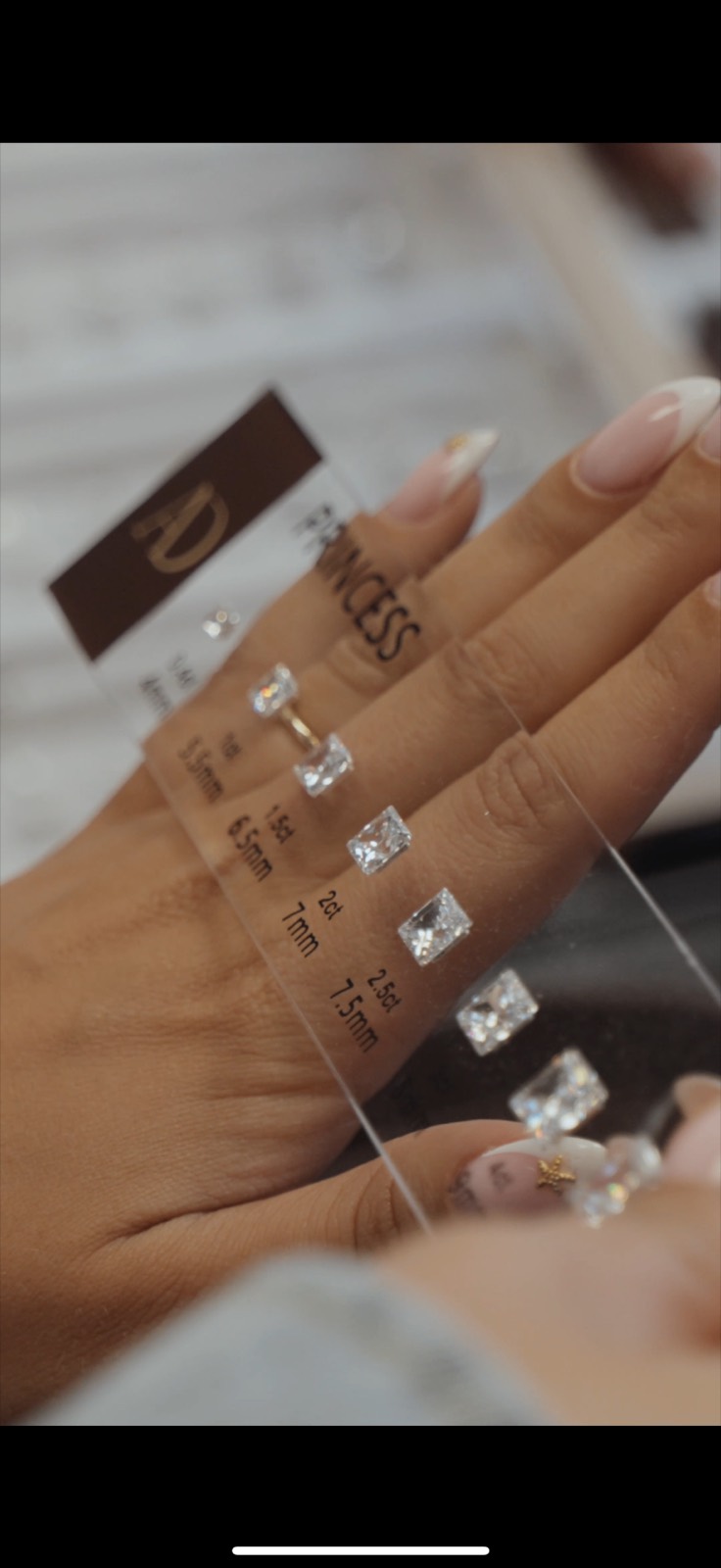 Clear sizing card of princess cut diamonds, labelled by carat and millimetre, held over a hand