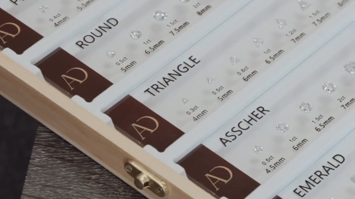 Diamond shape samples in a display case, labelled round, triangle, asscher and emerald with carat and millimetre sizes