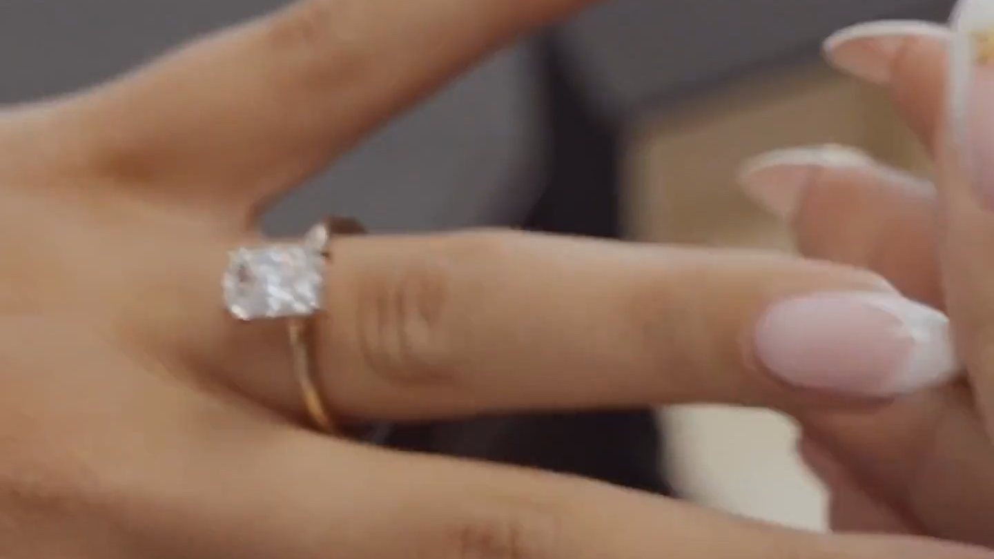 Radiant cut diamond solitaire engagement ring on a yellow gold band, worn on the hand