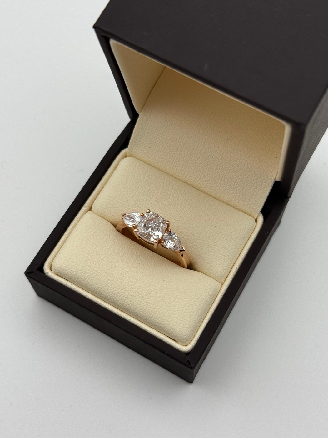 Rose gold trilogy engagement ring with a cushion cut centre and pear side stones, in a presentation box