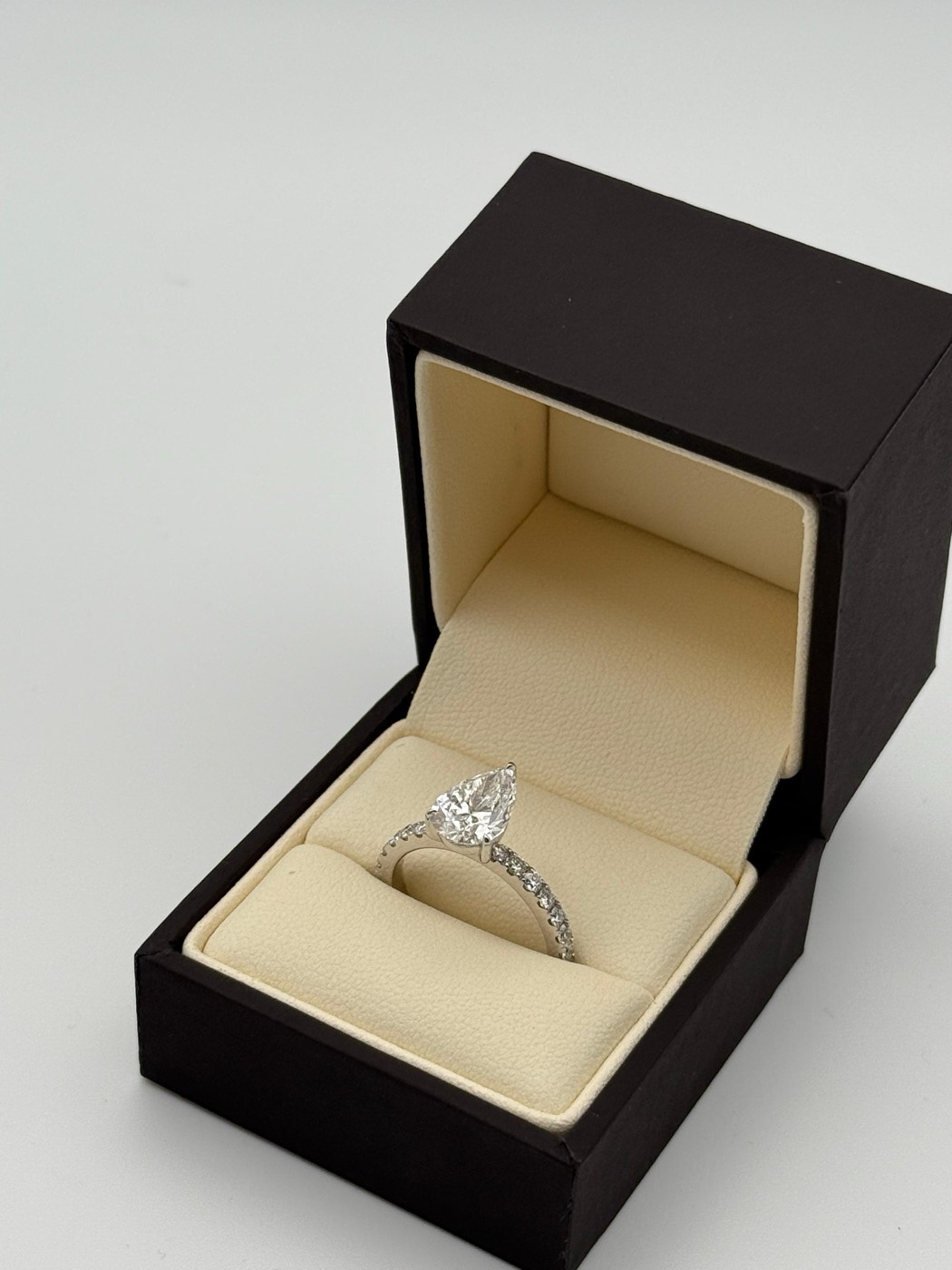 White gold pear cut engagement ring with a diamond pavé band, in a presentation box